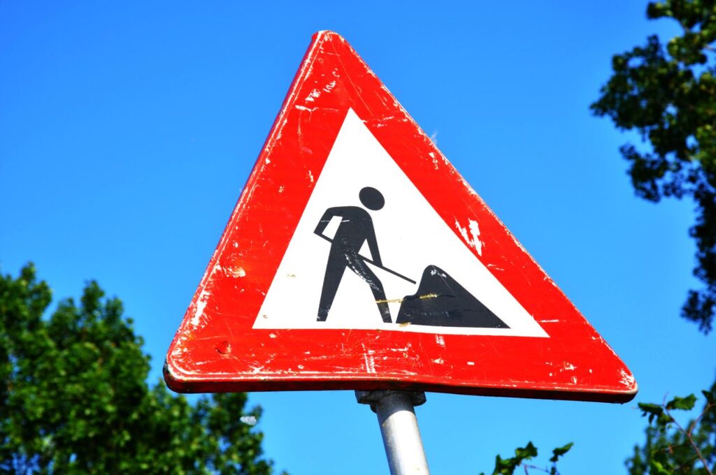 La CPTS A red and white roadwork warning sign with a silhouette figure, set against a clear blue sky.